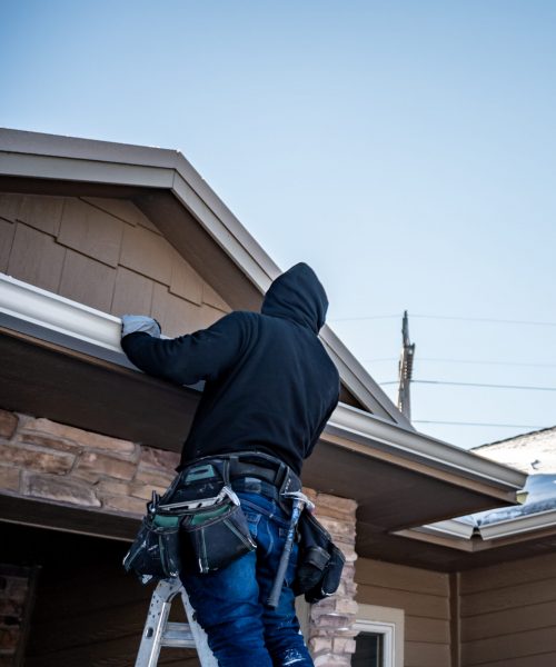 contractor installing gutters on a residential building in the winter with snow on the roof.